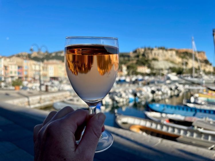 Weibliche Hand, die ein Glas Rosenwein hält, Hafen und Altstadt von Cassis im Hintergrund